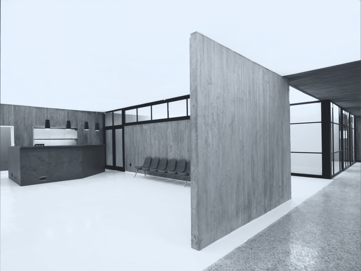 Empty clinic waiting area: board-formed concrete, a dark stone reception counter, a row of grey chairs