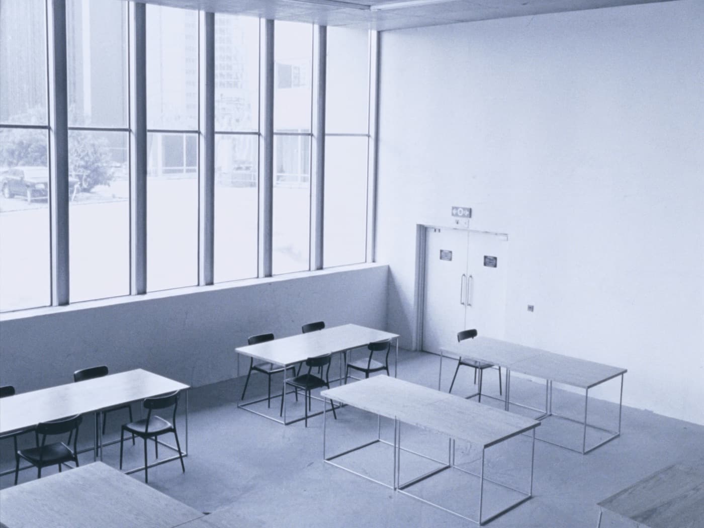 Empty contemporary dining room: pale plaster, oak tables in a grid, tall steel-framed windows